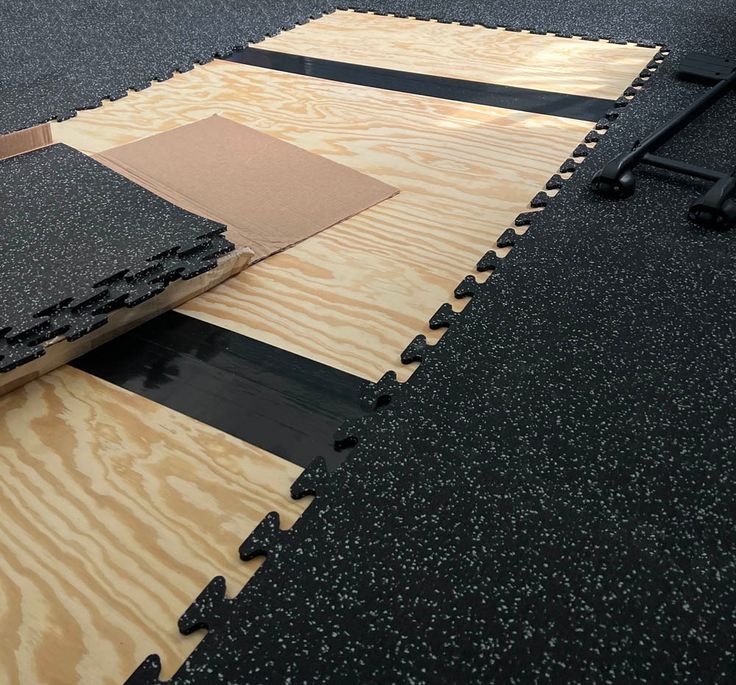 Interlocking rubber gym floor tiles being installed on a plywood base