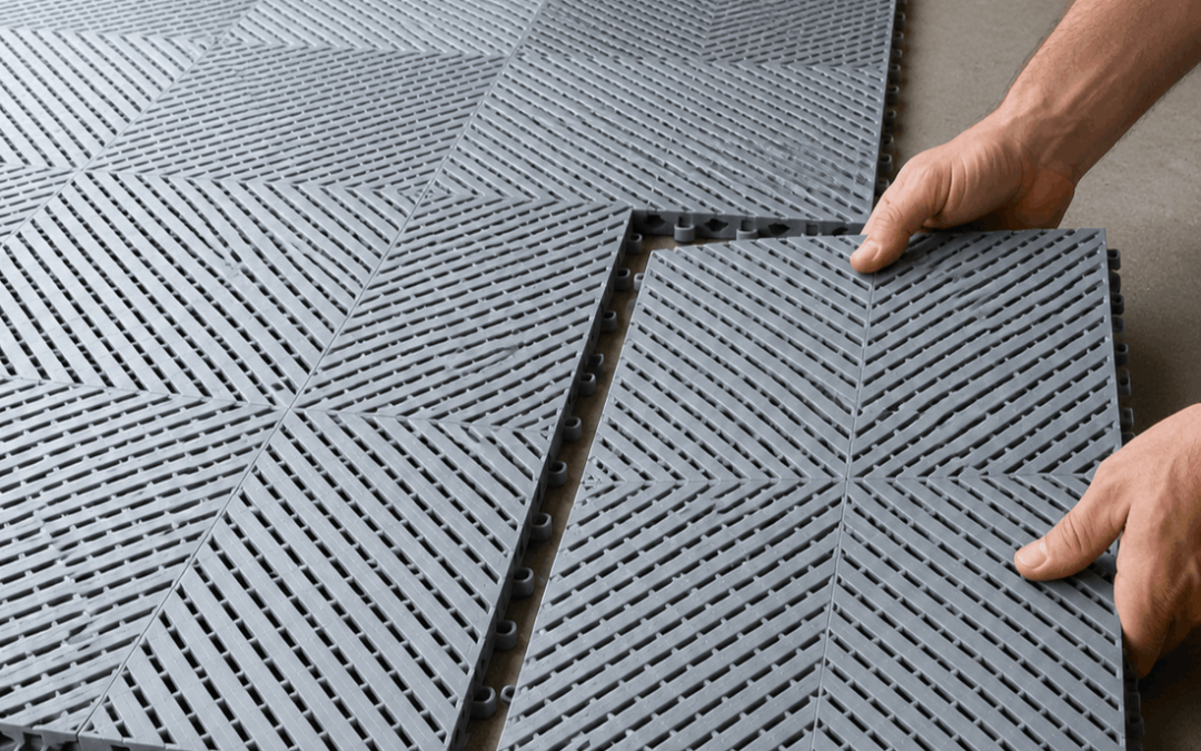 Person installing grey interlocking garage tiles without glue on a concrete floor