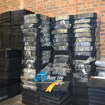 Stacks of black interlocking PVC floor tiles stored inside a warehouse